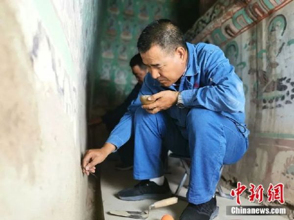 图为敦煌壁画“医生”修复壁画，窟外气温高达三四十度时，他们仍旧需要穿厚实的夹克，戴护膝和护腰。(资料图)