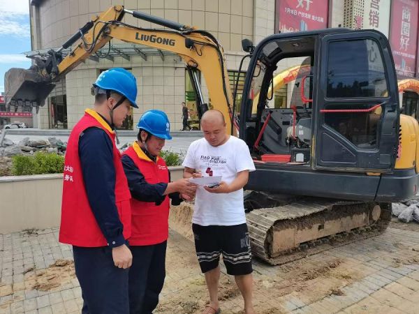 国网大连市普兰店供电公司员工李林、毕宝家在普兰店区站前广场对挖掘机施工人员讲解电力设施防外破知识。